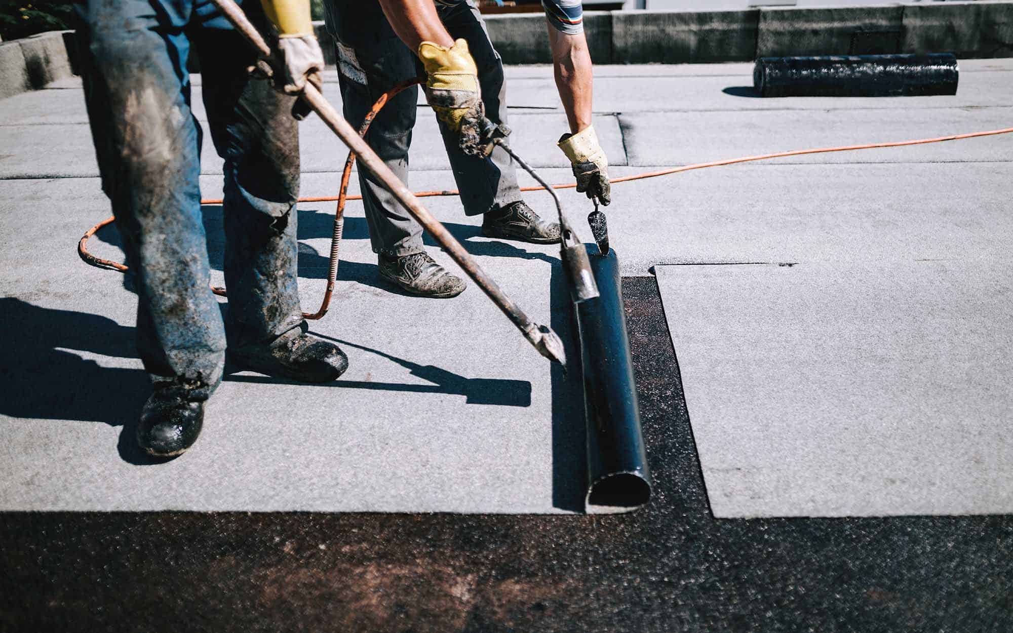 Two-roofers-applying-a-layer-of-asphalt-roofing